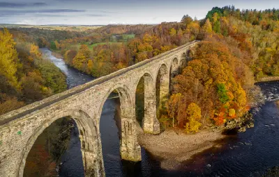 Aerial view of Lambley Viaduct crossing the River South Tyne, with tall stone arches, dark river waters and colourful autumn woodland in Northumberland.