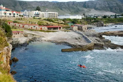 Historic stone harbour buildings and rocky shoreline at Old Harbour Hermanus with kayakers on the ocean in South Africa.