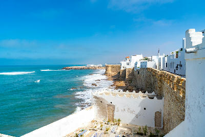 Whitewashed fortified walls of Asilah extend along Morocco’s Atlantic coastline beside the exposed ocean shoreline.