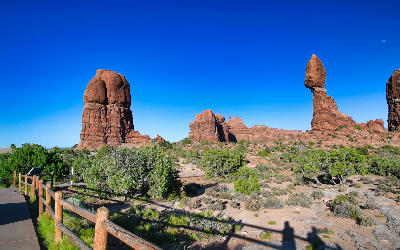 Balanced Rock formation with nearby sandstone towers and desert vegetation under clear blue sky in Arches National Park Utah