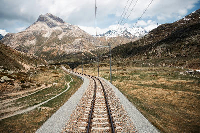 Railway tracks curving through an alpine valley with rugged mountains and overhead lines in the Swiss Alps