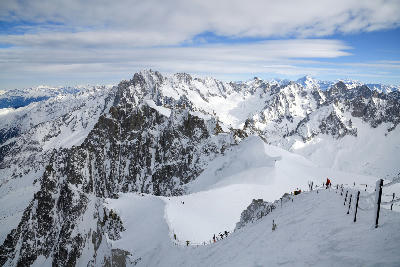 Climbers and skiers on a narrow ridge below Aiguille du Midi above the Mont Blanc Massif.