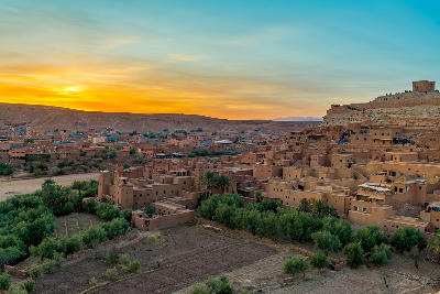 Aït Benhaddou fortified settlement at sunset in Morocco with oasis vegetation, agricultural fields, and desert plateau landscapes