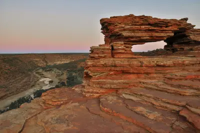 Layered red sandstone arch of Nature’s Window overlooking the Murchison River gorge in soft dusk light.