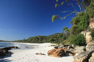 White sand, rocky shoreline and coastal bushland along Hyams Beach beside the blue waters of Jervis Bay.
