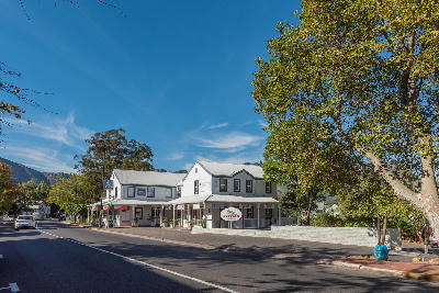 Historic Franschhoek railway station building with shops and cafés beside an oak-lined street in Franschhoek Village, Western Cape.