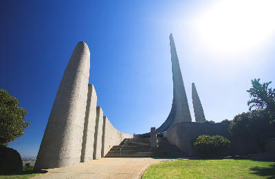 Modern concrete towers and curved architectural forms at the Afrikaans Language Monument in Paarl, South Africa, viewed under bright blue skies with landscaped gardens in the foreground.