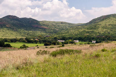 Rolling grassland hills and historic farm buildings in Suikerbosrand Nature Reserve beneath dramatic summer clouds.