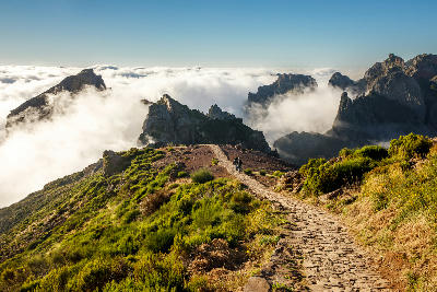 Mountain hiking trail near the summit of Pico do Arieiro, with stone path winding through rugged peaks above a sea of clouds.
