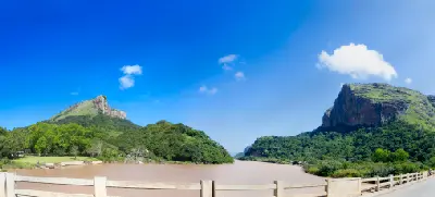 The Mzimvubu River winding between the forested cliffs of Port St Johns on the Wild Coast, Eastern Cape, South Africa, viewed from a bridge beneath a clear blue sky.