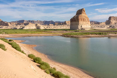 Lone Rock at Lake Powell in Wahweap Bay near Page, Arizona, showing a sandstone monolith beside a sandy lakeshore and calm reservoir water.