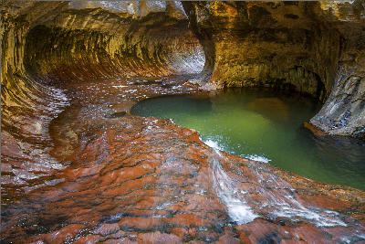 Curved sandstone tunnel with flowing water and green pool in The Subway canyon, Zion National Park