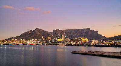 V&A Waterfront harbour at sunset with Table Mountain forming a flat-topped backdrop above Cape Town, South Africa.