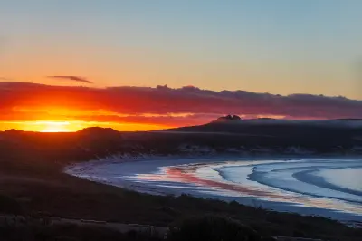 Sunrise over Lucky Bay with breaking waves and distant granite peaks in Cape Le Grand National Park, Western Australia.
