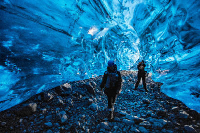 Tourists exploring a vivid blue ice cave under Vatnajökull Glacier in Iceland.