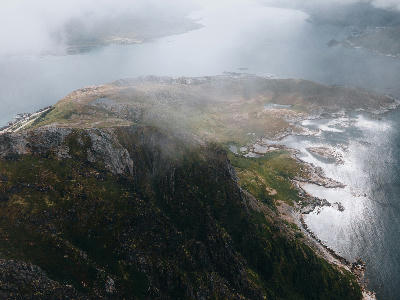 Elevated view from Offersøykammen on Vestvågøya in the Lofoten Islands, showing steep cliffs descending to turquoise coastal waters and rocky shoreline in Norway.