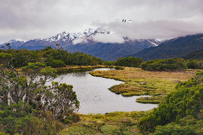 Alpine wetland pond at Key Summit with snow-covered mountains and low clouds in Fiordland National Park, New Zealand.