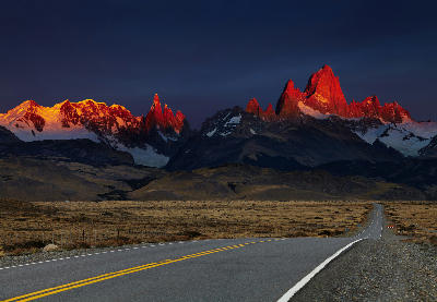 Road leading toward Mount Fitz Roy at sunrise with red alpenglow on peaks in Patagonia, Argentina.