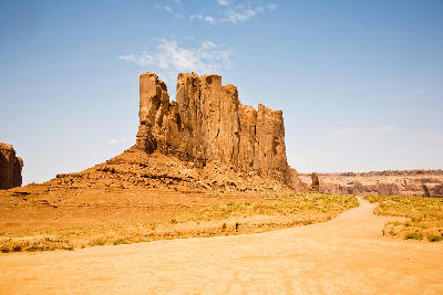 Camel Butte sandstone formation in Monument Valley with desert road and dry landscape under clear sky