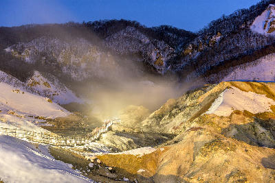Illuminated boardwalk through steaming geothermal valley at Jigokudani Hell Valley in winter, Noboribetsu, Hokkaido, Japan.