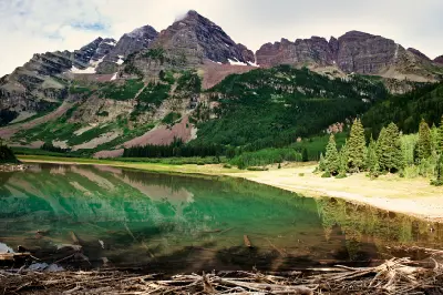 Crater Lake near Aspen Colorado reflecting the Maroon Bells with clear water, submerged logs, and forested mountain slopes in the Elk Mountains.