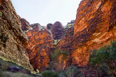 Towering orange-and-black striped sandstone walls and rounded domes rise above native vegetation in the Bungle Bungle Range.