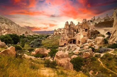 Ancient cave houses carved into volcanic rock at Zelve Open Air Museum in Cappadocia, Turkey, surrounded by dramatic valleys and fairy chimney formations beneath a colourful sunset sky.