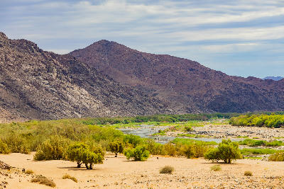 The Orange River flowing through Richtersveld National Park, with green riverbank vegetation framed by rugged desert mountains in the Northern Cape.