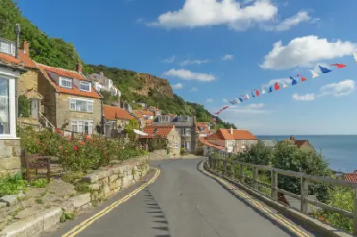 Curving village street lined with stone cottages, red-tiled roofs, flowers and colourful bunting, overlooking the sea at Runswick Bay, North Yorkshire.