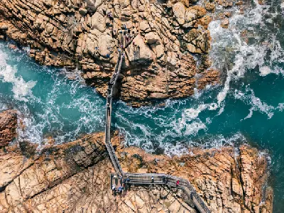 Aerial view of visitors crossing the Canal Rocks footbridge above turquoise water and rugged granite formations near Yallingup, Western Australia.