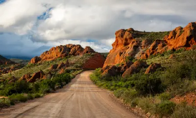 Gravel road passing through dramatic red sandstone outcrops at Red Stone Hills near Calitzdorp, surrounded by Karoo vegetation beneath moody clouds in the Klein Karoo, South Africa.