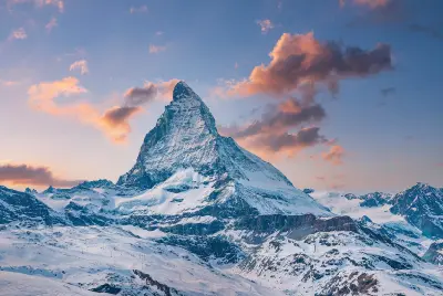Matterhorn peak above Zermatt with snow-covered slopes and soft pink clouds at sunset, Swiss Alps
