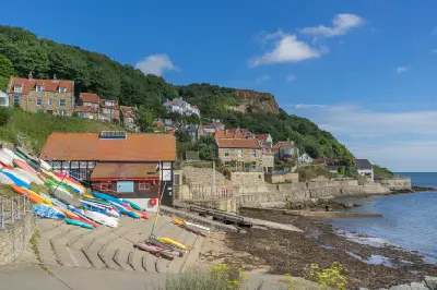 Colourful kayaks and small boats beside the waterfront at Runswick Bay, with traditional stone cottages on a green hillside overlooking the North Sea in Yorkshire, England.