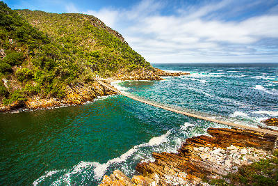 Suspension bridge spanning Storms River Mouth above turquoise water and rocky cliffs in Tsitsikamma National Park, South Africa.