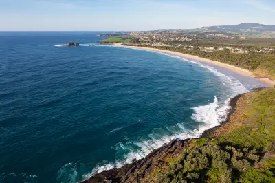 Aerial view along Minnamurra Beach with waves breaking onto the long sandy shoreline, Rangoon Island offshore and the Kiama coastline stretching into the distance.