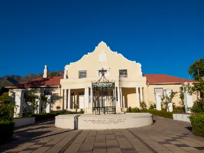 Cape Dutch-style Huguenot Memorial Museum building in Franschhoek with mountain backdrop in the Cape Winelands of South Africa.