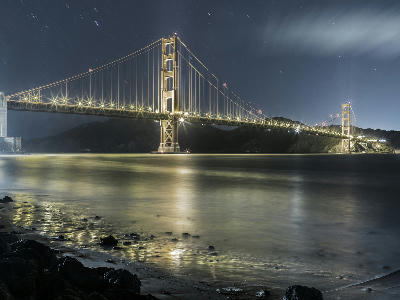 Golden Gate Bridge illuminated at night from Hawk Hill with long exposure water and star trails, San Francisco, California