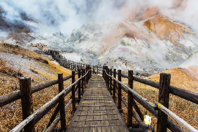 Wooden boardwalk leading through the steaming geothermal landscape of Jigokudani Hell Valley in Noboribetsu, Hokkaido.