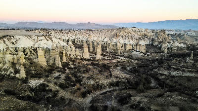 Aerial panorama of Love Valley in Cappadocia, Turkey, featuring towering fairy chimney rock formations sculpted from volcanic tuff at sunrise.