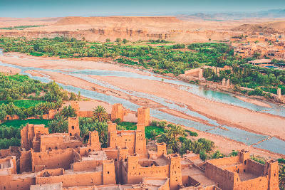 Fortified desert settlement near Ouarzazate, Morocco with river valley, oasis vegetation, and earthen kasbah architecture at golden hour