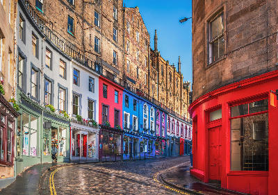 Rainy street scene on Victoria Street in Edinburgh, with colourful building facades and wet cobblestones reflecting light.