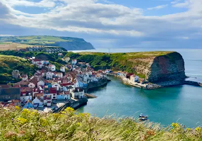 Elevated view of Staithes fishing village in North Yorkshire, showing red-roofed cottages, a sheltered harbour, green coastal cliffs and the North Sea.