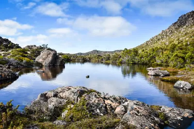 Calm waters of Johnston Tarn surrounded by alpine vegetation and rocky highlands on the Tarn Shelf in Mount Field National Park, Tasmania.