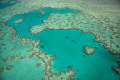 Wide aerial view of Heart Reef surrounded by turquoise lagoons and extensive coral formations in the Great Barrier Reef, Queensland.