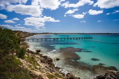 Wooden Vivonne Bay Jetty extending across turquoise water with dark reef patches, rocky shoreline and coastal vegetation on Kangaroo Island, South Australia.