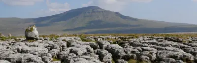 Fractured limestone pavement and an isolated boulder on Scales Moor, with Ingleborough mountain in the background, Yorkshire Dales, England.