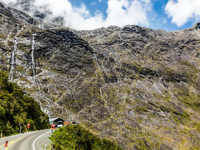 Road entering the Homer Tunnel beneath steep cliffs and waterfalls on State Highway 94 in Fiordland National Park, New Zealand.