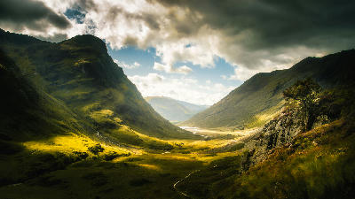 Green-covered hills surrounding Glen Coe village in the Scottish Highlands, with rolling slopes and soft natural light.