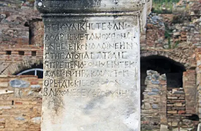 Close-up of an ancient Greek inscription carved into a weathered marble pillar among the ruins along Curetes Street in Ephesus.