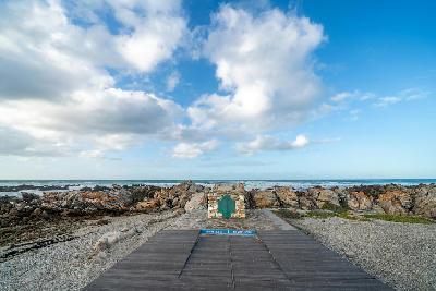 Cape Agulhas southern tip marker surrounded by rocky coastline and ocean under dramatic clouds in South Africa.